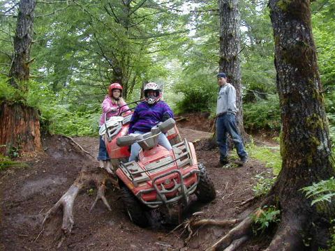 1994 Ford Explorer - Two people ride an ATV through a wooded area with a third person standing in the background.