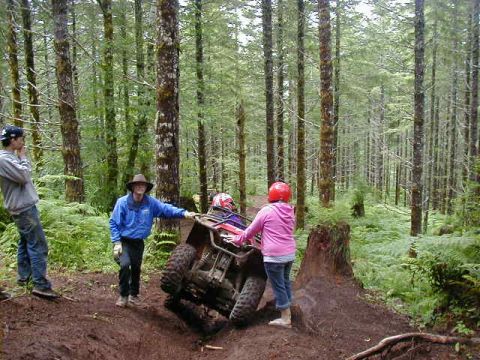 1994 Ford Explorer - An ATV is stuck on a dirt trail surrounded by trees, with three people observing the situation.