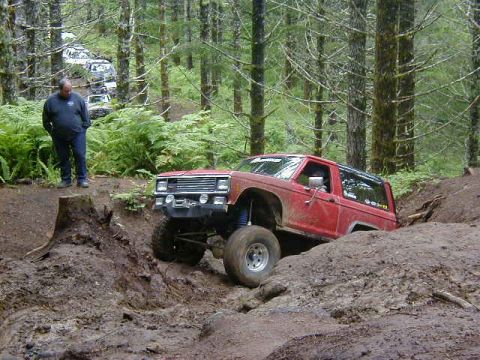 1994 Ford Explorer - A red off-road SUV navigates a challenging muddy terrain, with other vehicles following on a wooded trail.