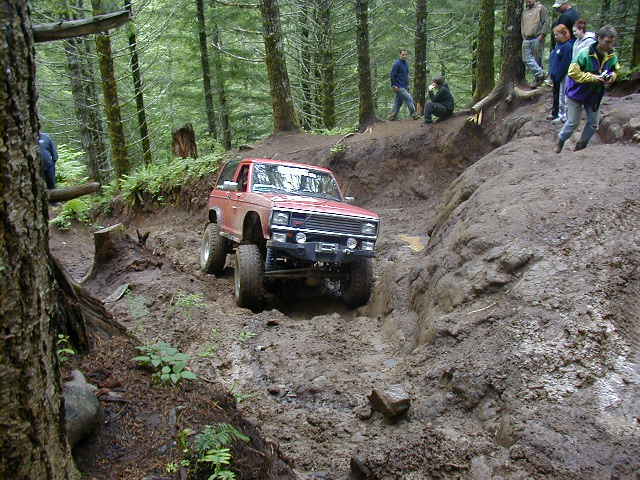 Red SUV navigating a steep, muddy off-road trail with onlookers