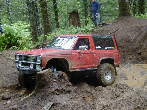 1994 Ford Explorer - This red Ford Bronco II is navigating a challenging muddy trail in a wooded area.