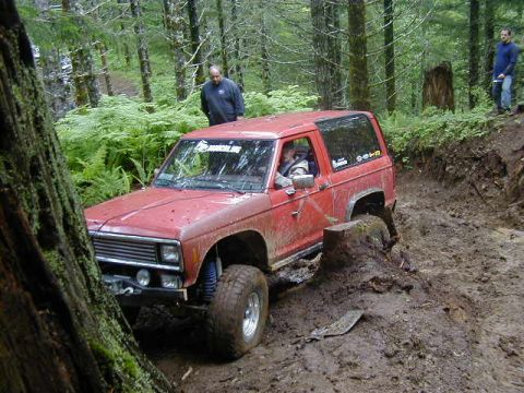 1994 Ford Explorer - A red off-road vehicle navigates a challenging muddy terrain with onlookers present.