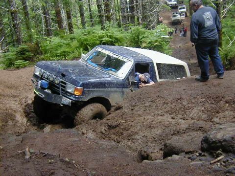 1994 Ford Explorer - An off-road vehicle navigates a challenging muddy terrain, with other vehicles visible further up the trail.