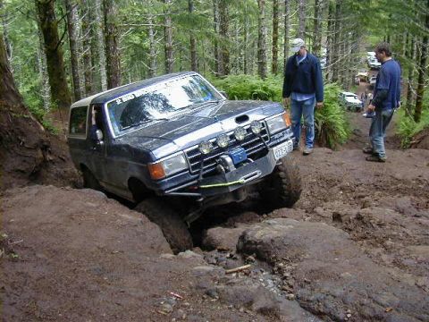 1994 Ford Explorer - An off-road vehicle navigates a challenging, muddy terrain with spectators observing the action.