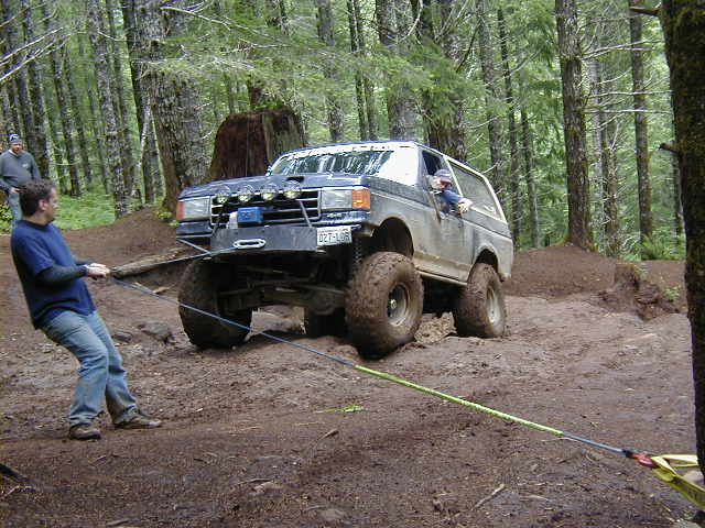 Dark blue Ford Bronco with large tires, being pulled by a man in a blue shirt
