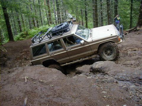 1994 Ford Explorer - An SUV navigates a challenging muddy off-road course in a wooded area.