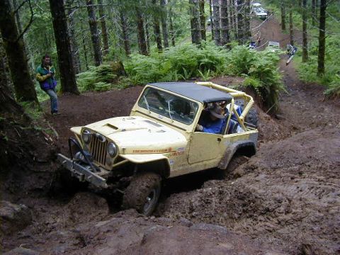 1994 Ford Explorer - A yellow Jeep Wrangler struggles through a deep mud pit on a wooded trail.