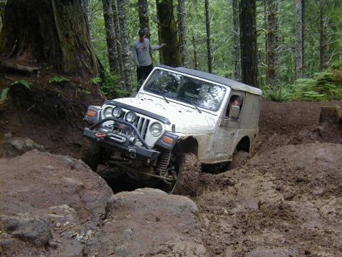 1994 Ford Explorer - A white Jeep Wrangler navigates a difficult muddy obstacle on an off-road trail.
