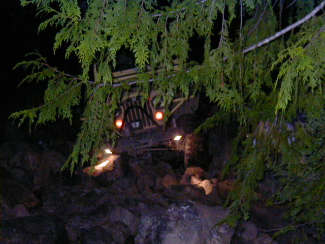 4x4 headlights glowing through evergreen branches while night-crawling a dark rocky trail