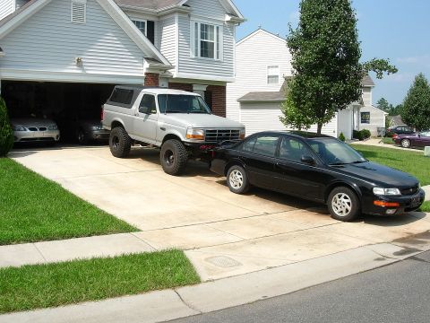 1995 Ford Bronco - A lifted 1995 Ford Bronco is hitched to a black sedan in a suburban driveway.