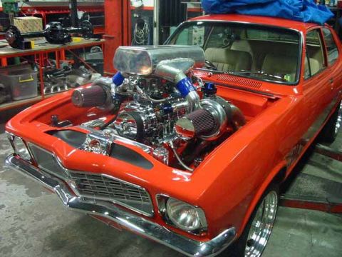 1990 Ford Bronco - orange classic sedan in a workshop displays a massive supercharged V8 with a blower poking through the hood.