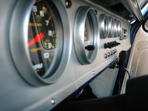 1978 Ford Bronco - The dashboard features several gauges and switches, with a reflection of trees visible in the RPM gauge.