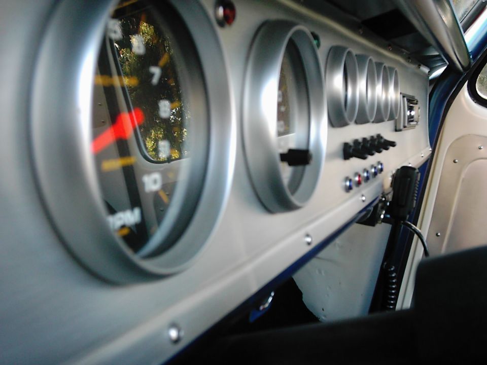 Close-up of a vehicle's dashboard with multiple gauges, including a prominent RPM meter. Switches and indicator lights are also visible