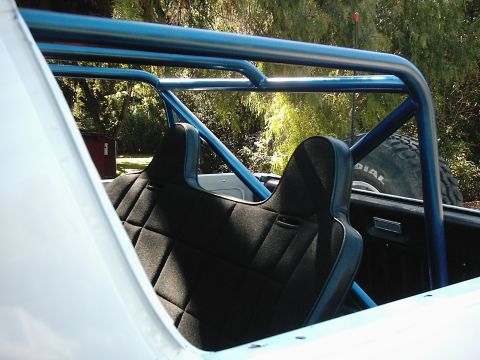 1978 Ford Bronco - The interior of a vehicle shows black quilted seats and a blue roll cage, with a spare tire visible in the background.