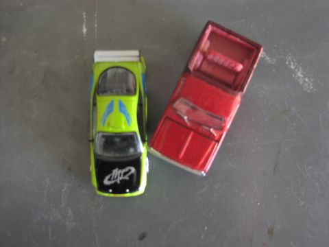 1979 Ford Bronco - A pair of toy cars, one a green sports car with racing stripes and the other a red pickup truck, sit on a textured surface.