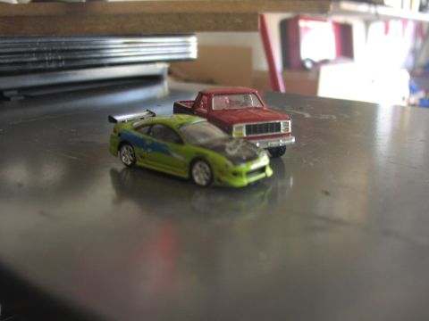 1979 Ford Bronco - Two miniature toy vehicles are positioned on a shiny surface, with a shelf in the background.