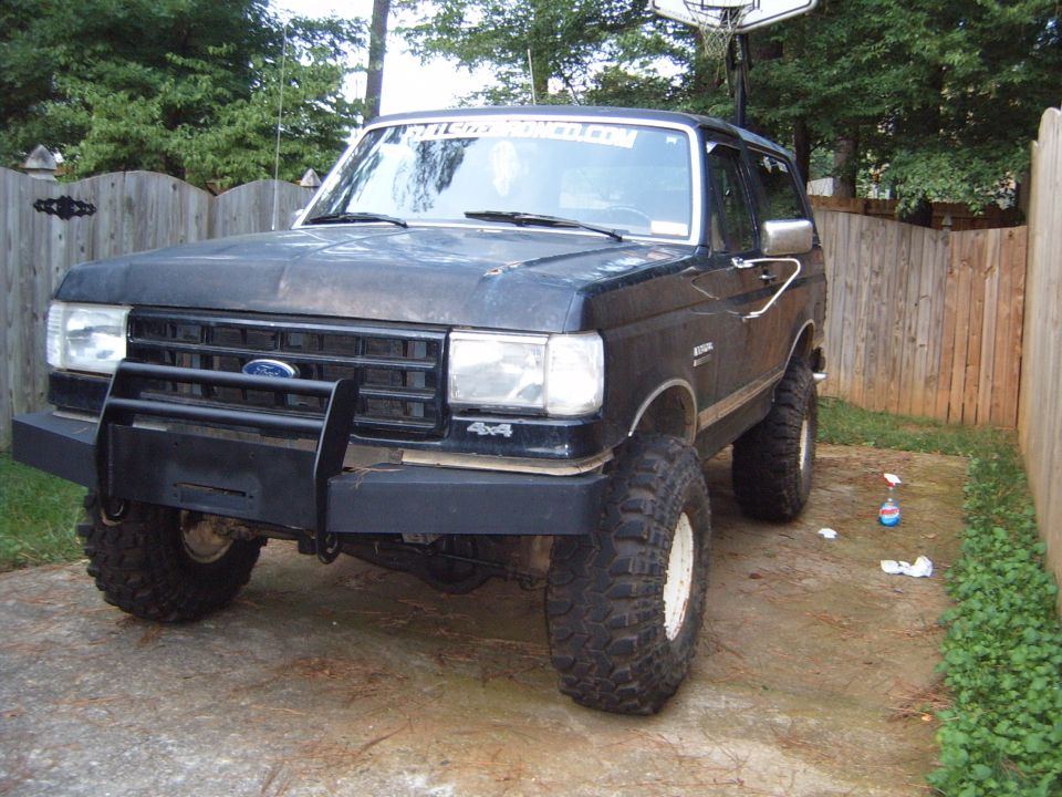 Black Ford Bronco with aftermarket bumper and large tires, parked in a driveway