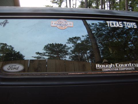 1988 Ford Bronco - Rear window of a Ford Bronco displays 'Texas Toys' and 'Rough Country Competition Components' stickers, along with a Ford oval badge.