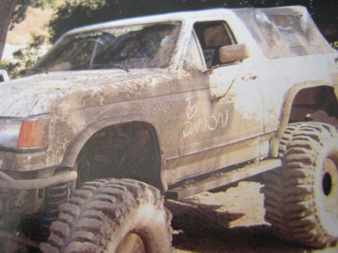 1990 Ford Bronco - heavily mud-covered lifted white two-door SUV sits on oversized off-road tires with handwriting on its door.
