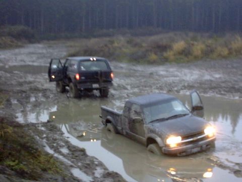 1995 Ford Bronco - Two SUVs are deeply stuck in a muddy, waterlogged area, with one vehicle's doors open.