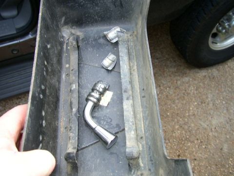 1995 Ford Bronco - Close-up of a broken lug wrench part and two caps within a black plastic trim piece.