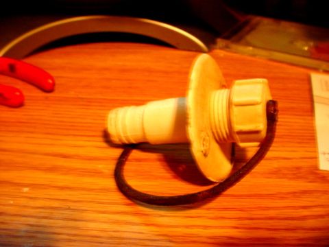 1973 Ford Ranchero - A radiator cap with a tether is shown on a wooden table, with a partial view of red objects and a white curved edge.