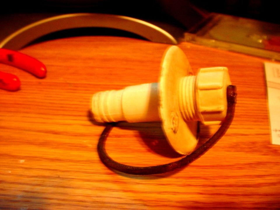 White plastic radiator cap with a black tether, resting on a wooden surface