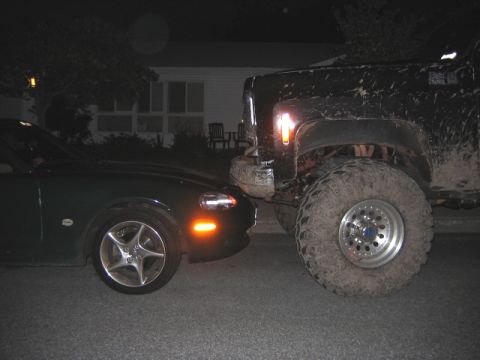 1976 GMC C/K Pickup - A large, muddy pickup truck is parked very close to a dark sports car at night.