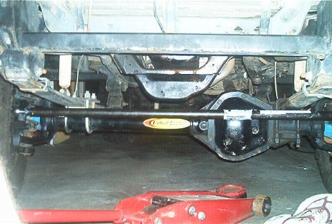 1986 Ford Bronco - Undercarriage view of steering linkage, a Detroit Locker component and part of a red hydraulic jack.