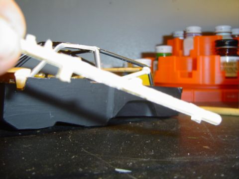 1979 Ford Bronco - A person attaches a white plastic part to a model car chassis with a visible roll cage.