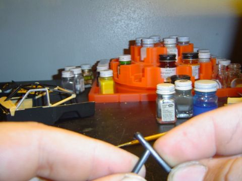 1979 Ford Bronco - A model car chassis is seen on a workbench alongside numerous small bottles of paint.