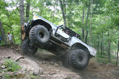 1999 Jeep TJ - This heavily modified off-road vehicle navigates a challenging, steep, and rocky trail through a wooded area.
