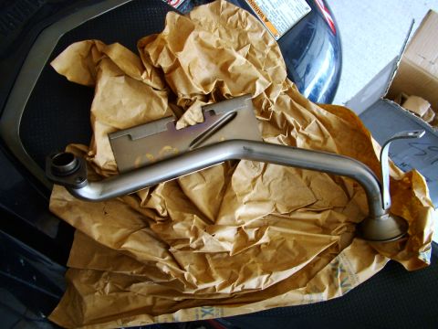 2003 Ford Mustang - A metal oil pickup tube is shown, partially wrapped in brown paper, with a cardboard box visible.