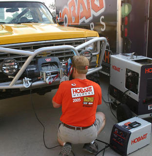 1999 Jeep TJ - A man wearing a Hobart Welders shirt works on a yellow off-road vehicle, possibly modifying its front bumper for an adventure.