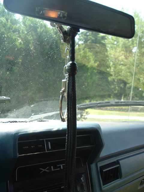 1989 Ford Bronco - Interior view looking forward from behind the rear-view mirror of an older Ford truck, with a braided black leather whip or tassel and a pa…