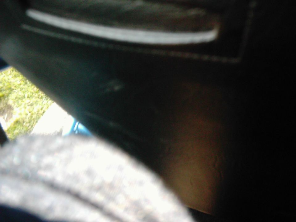 Interior view of a dark vehicle with a blurry grey seat in the foreground and a glimpse of green foliage outside