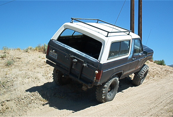 1980s Ford Bronco with a white top and dark body driving on a dirt hill