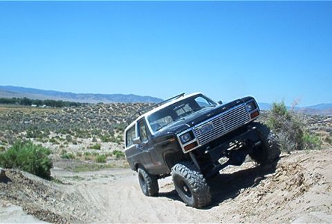 1986 Ford Bronco - A modified Ford Bronco navigates an off-road trail under a clear blue sky.