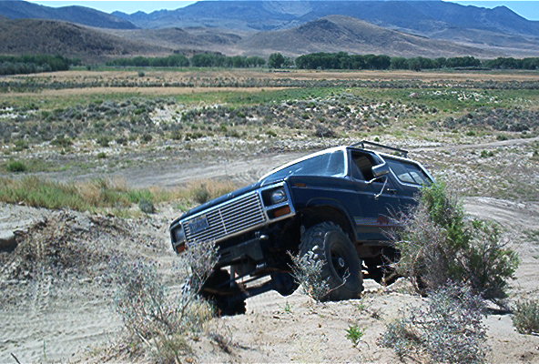Dark blue 1980s Ford Bronco off-roading in a dry, hilly landscape