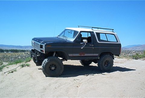 1986 Ford Bronco - This modified Ford Bronco is shown off-road under a clear blue sky.