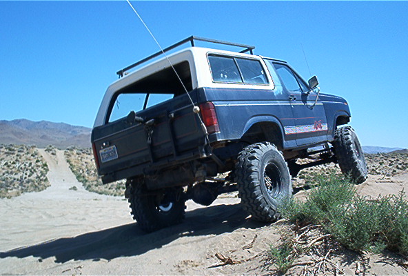 1986 Ford Bronco with lifted suspension and large tires driving on sand dunes