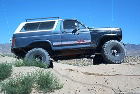 1986 Ford Bronco - This modified Ford Bronco is navigating a sandy, off-road trail under a clear blue sky.