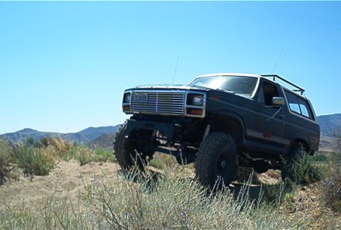 1986 Ford Bronco - This modified Ford Bronco navigates a dusty, arid landscape with mountains in the background.