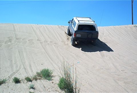 1986 Ford Bronco - A Ford Bronco navigates a steep sand dune on a sunny day.