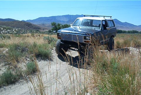 1986 Ford Bronco - This 1986 Ford Bronco is shown off-roading in a dry, hilly landscape under a clear blue sky.