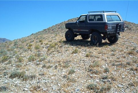 1986 Ford Bronco - This modified Ford Bronco is navigating a steep, arid hillside on a clear day.