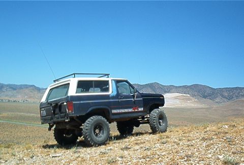 1986 Ford Bronco - Modified Ford Bronco with off-road tires sits on a hillside with mountains in the background.