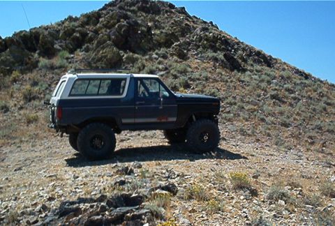 1986 Ford Bronco - Ford Bronco navigates a steep, rocky terrain under a clear blue sky.