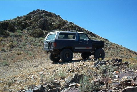 1986 Ford Bronco - This modified Ford Bronco is navigating a steep, rocky incline under a clear blue sky.