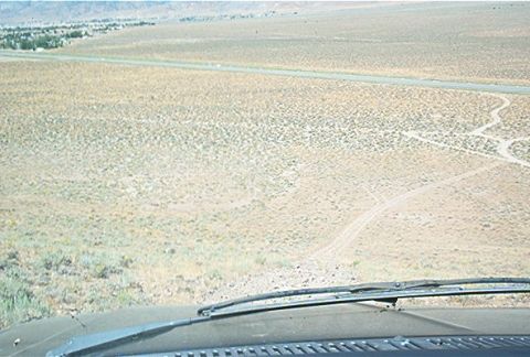 1986 Ford Bronco - View from inside a vehicle looking out over a vast, arid landscape with a distant road and tire tracks.